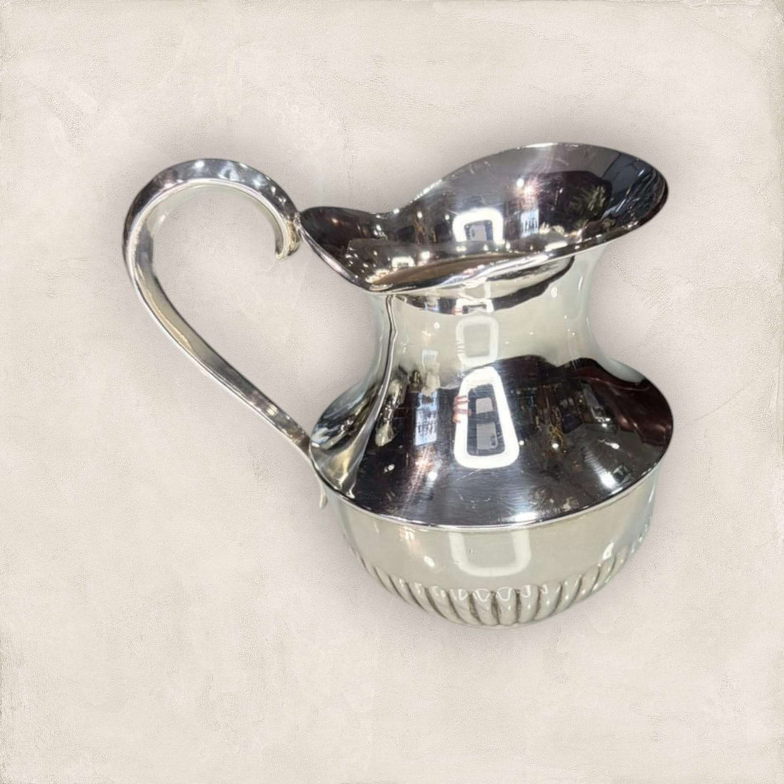 Jarra de metal plateado con acabado brillante y diseño curvo, ideal para decoración elegante en espacios del hogar.