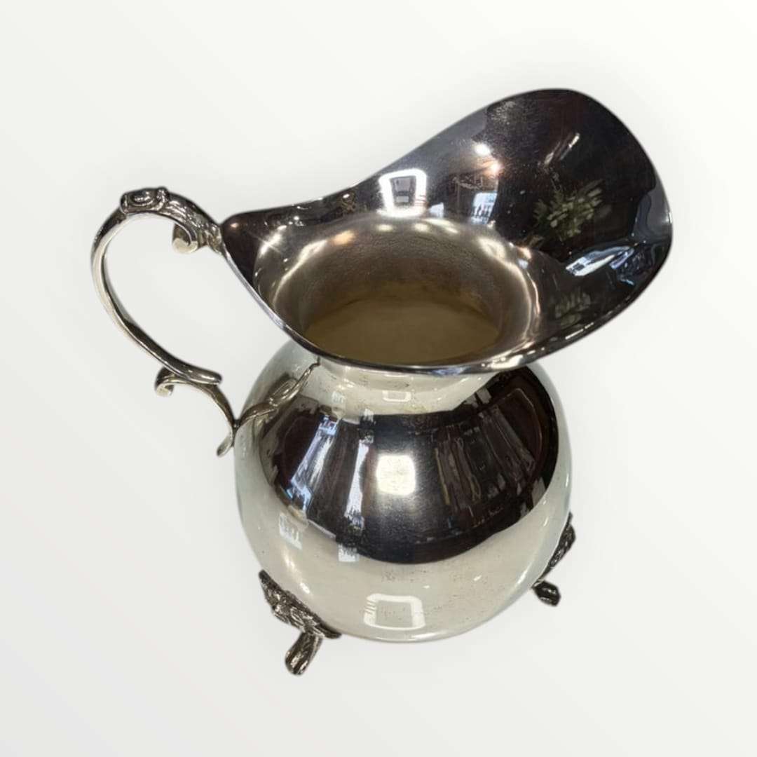 Jarra de metal plateado con diseño clásico y asa ornamentada, ideal para decoración elegante en el hogar. Pieza única de estilo intemporal.