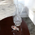Jarra licorera de cristal tallada con asa decorativa y tapa desmontada, perfecta para eventos especiales o como pieza decorativa.