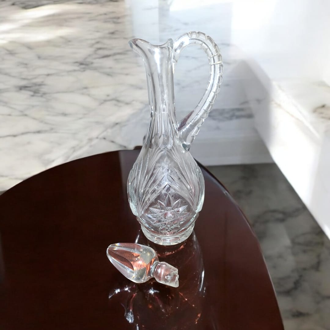 Jarra licorera de cristal tallada con asa decorativa y tapa desmontada, perfecta para eventos especiales o como pieza decorativa.