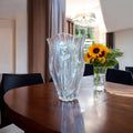 Jarrón de cristal tallado DARO con flor de plata de ley sobre mesa de comedor, complemento decorativo elegante para el hogar.