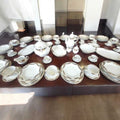 Vajilla de Bavaria, porcelana alemana – Juego completo de 107 piezas con platos, tazas, bandejas y teteras sobre mesa de madera oscura. Ideal para decoración de cocina elegante.