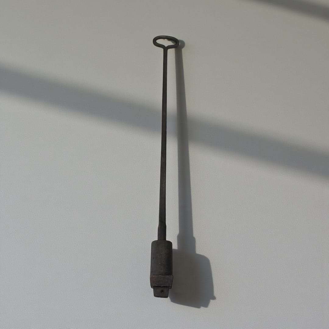Marcador tonelero antiguo de forja con letra P, pieza única de decoración rústica sobre fondo de madera con hojas verdes. Ideal para coleccionistas.