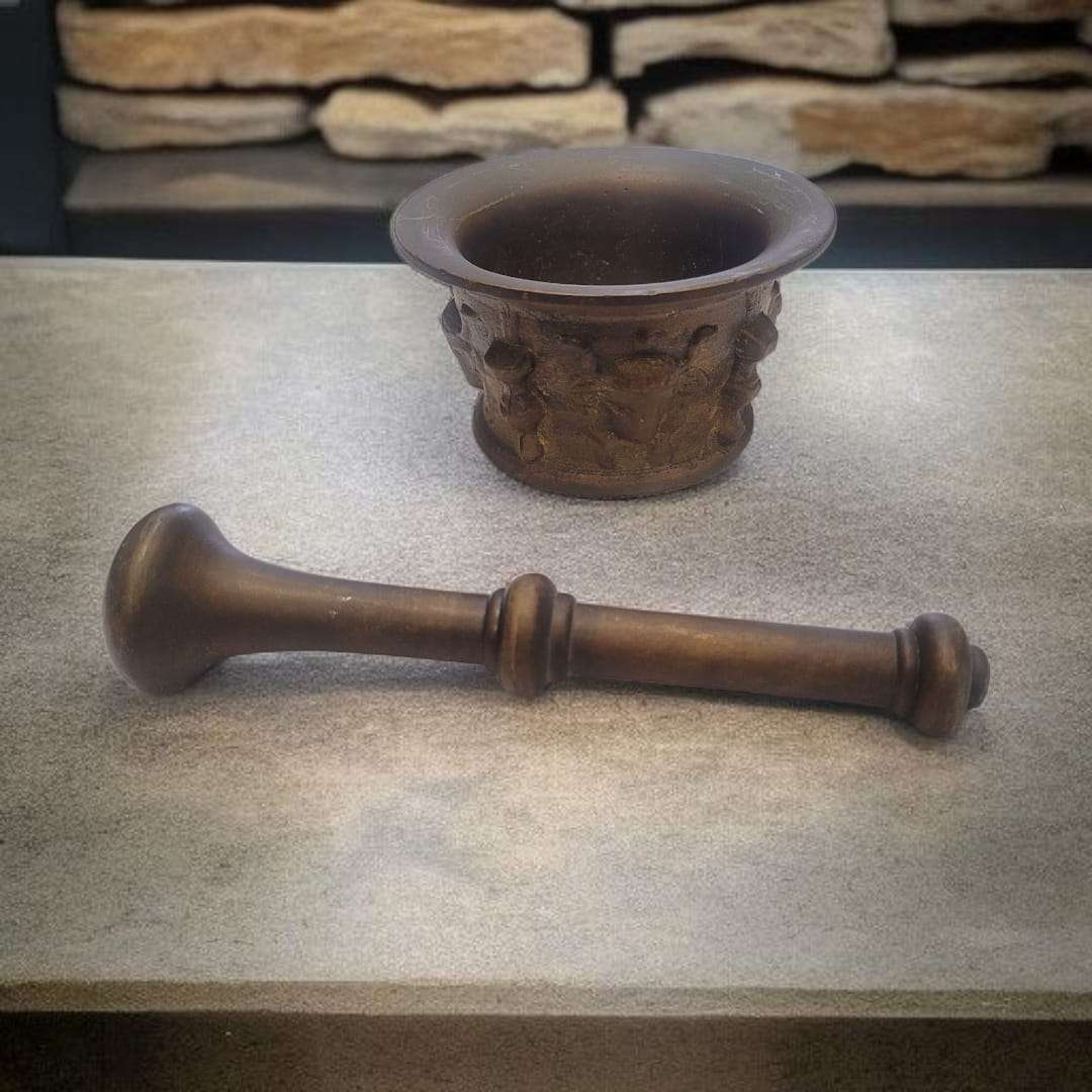 Mortero de bronce con grabados en relieve y maja separada. Pieza decorativa funcional para coleccionismo o uso culinario.