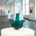 Pieza de Cristal Murano – Arte único para tu decoración en verde esmeralda con forma floral, expuesta sobre pedestal en galería de arte moderna.