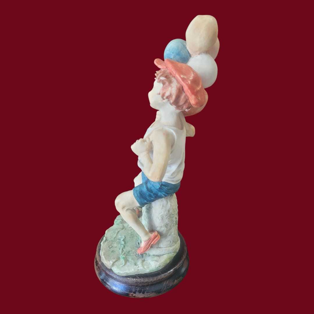 Figura decorativa niño con globos estilo Capodimonte vista en ángulo, con ropa veraniega y base de madera. Pieza única para colección.