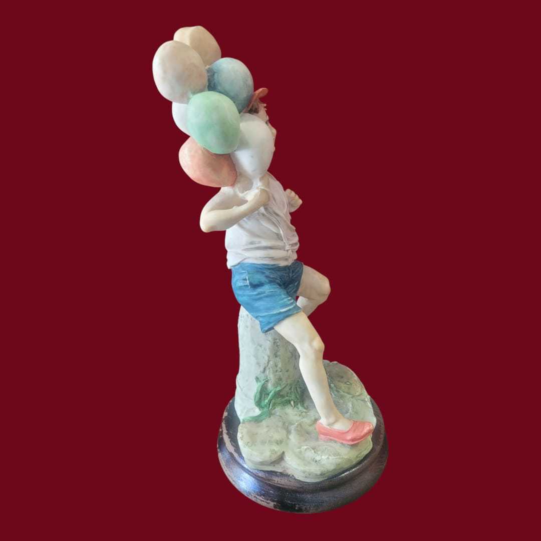 Figura niño con globos estilo Capodimonte sobre peana de madera, en resina colorida y alegre. Ideal para decoración de interiores exclusiva.
