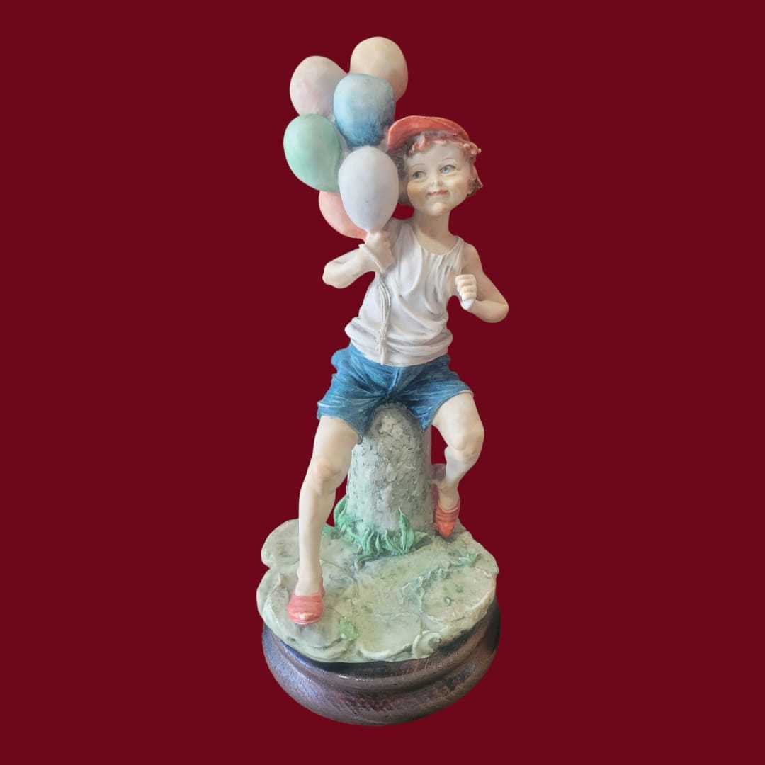 Figura niño con globos estilo Capodimonte sobre peana de madera, en resina colorida y alegre. Ideal para decoración de interiores exclusiva.