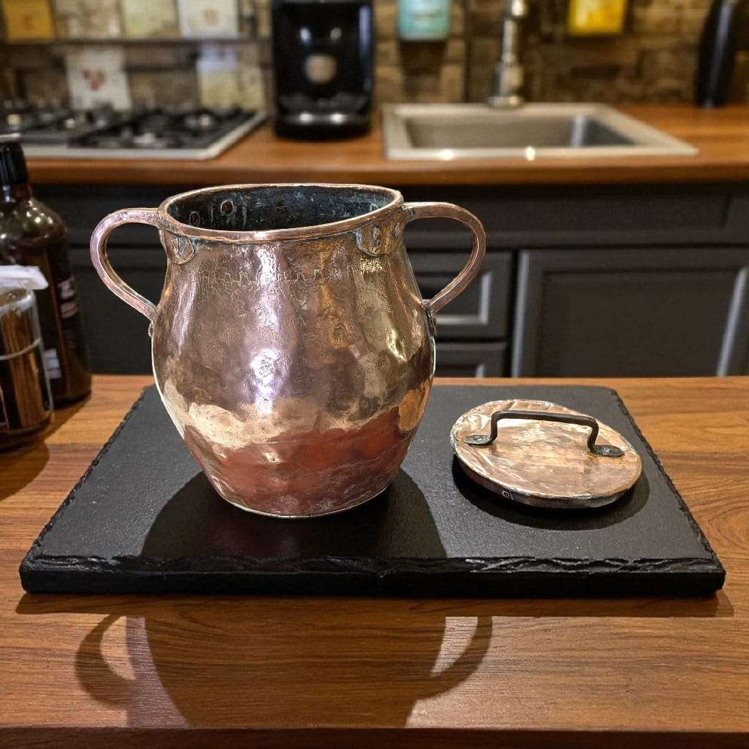 Olla de cobre antigua martilleada con tapa y asas, ideal para decoración rústica de cocina o colección vintage. Diseño artesanal y acabado brillante.