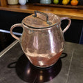 Olla de cobre antigua martilleada con tapa y asas, ideal para decoración rústica de cocina o colección vintage. Diseño artesanal y acabado brillante.