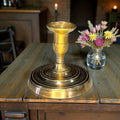 Palmatoria dorada vintage sin vela sobre mesa de madera, perfecta para ambientes rústicos y decoración de interiores elegante.