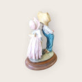 Figura de pareja infantil en resina sobre base de madera, mostrando un beso tímido desde ángulo posterior, perfecta para colecciones románticas.