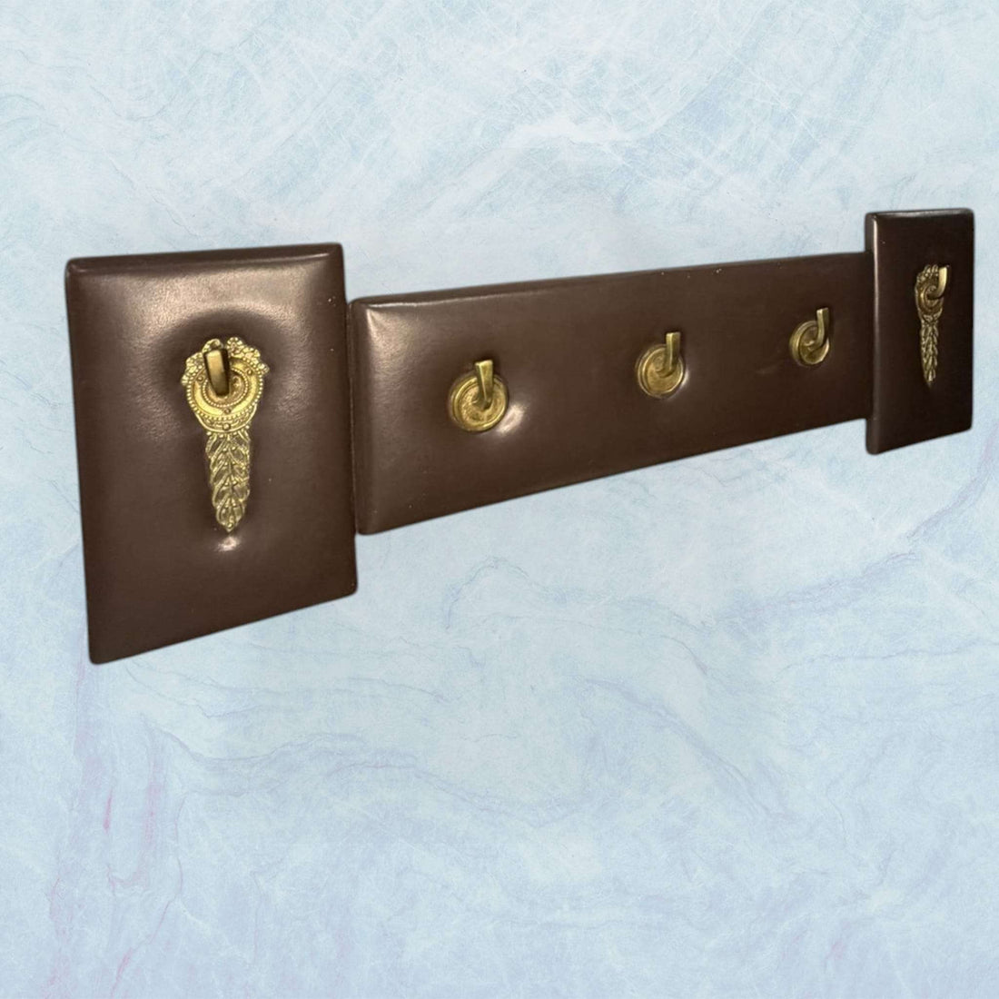 Perchero elegante de metal y cuero exclusivo y único con cuatro ganchos dorados y base marrón, ideal para decoración de interiores con estilo clásico.