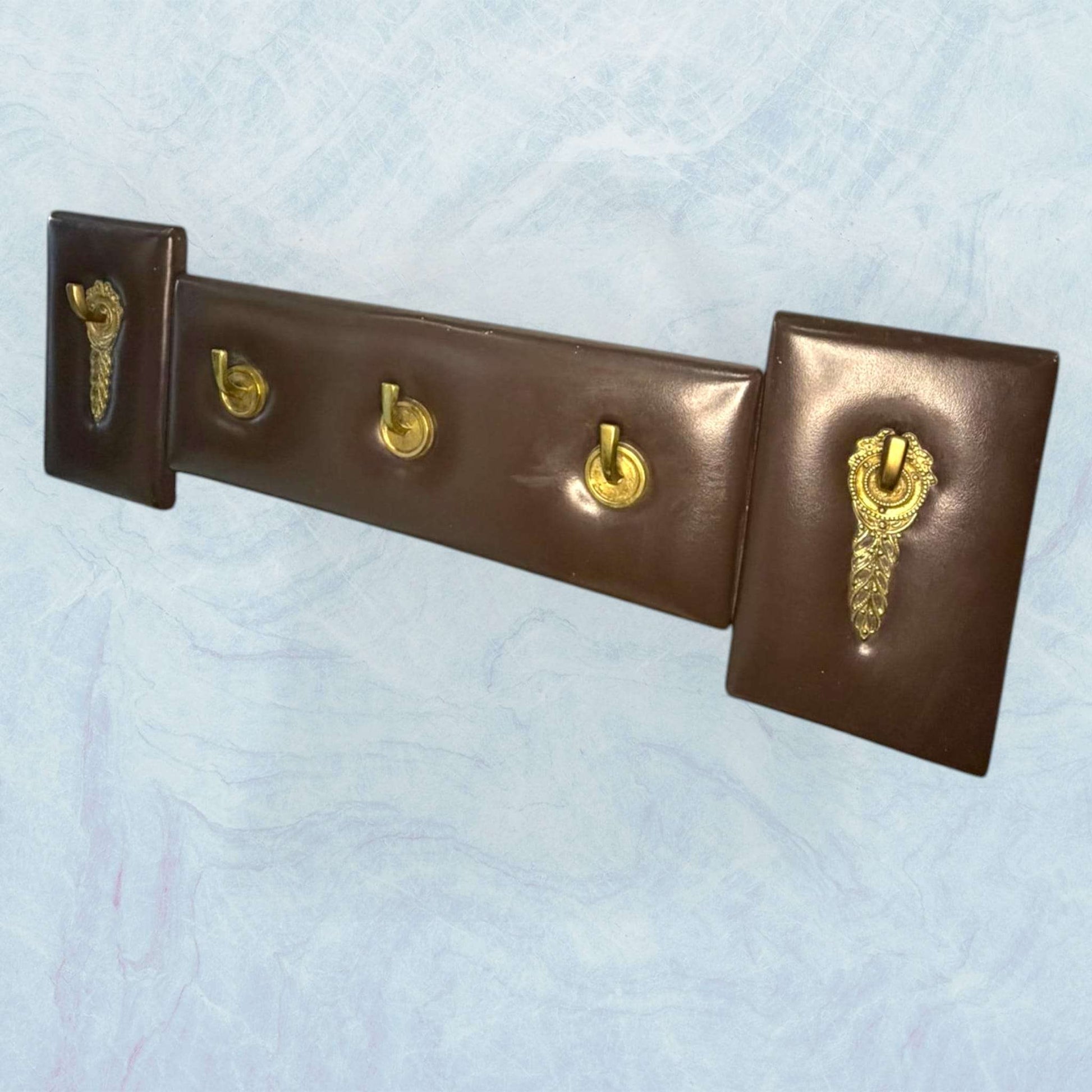 Perchero elegante de metal y cuero exclusivo y único con ganchos dorados sobre base acolchada marrón. Ideal para decoración de interiores con estilo.