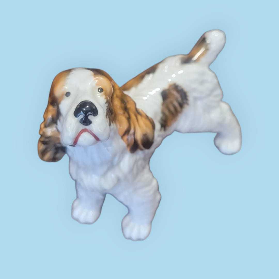 Figura coleccionista de perro Cocker de porcelana alemana Trébol años 50, esmaltada con detalles realistas en blanco y marrón.