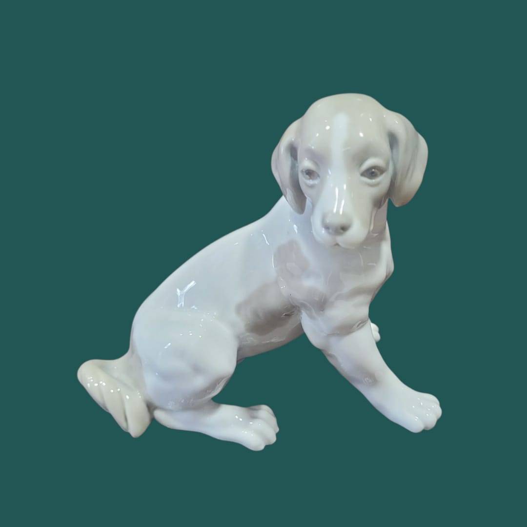 Figura perro NAO Lladró - Porcelana Cachorro Sentado en vista frontal, pieza decorativa de porcelana española con expresión tierna.