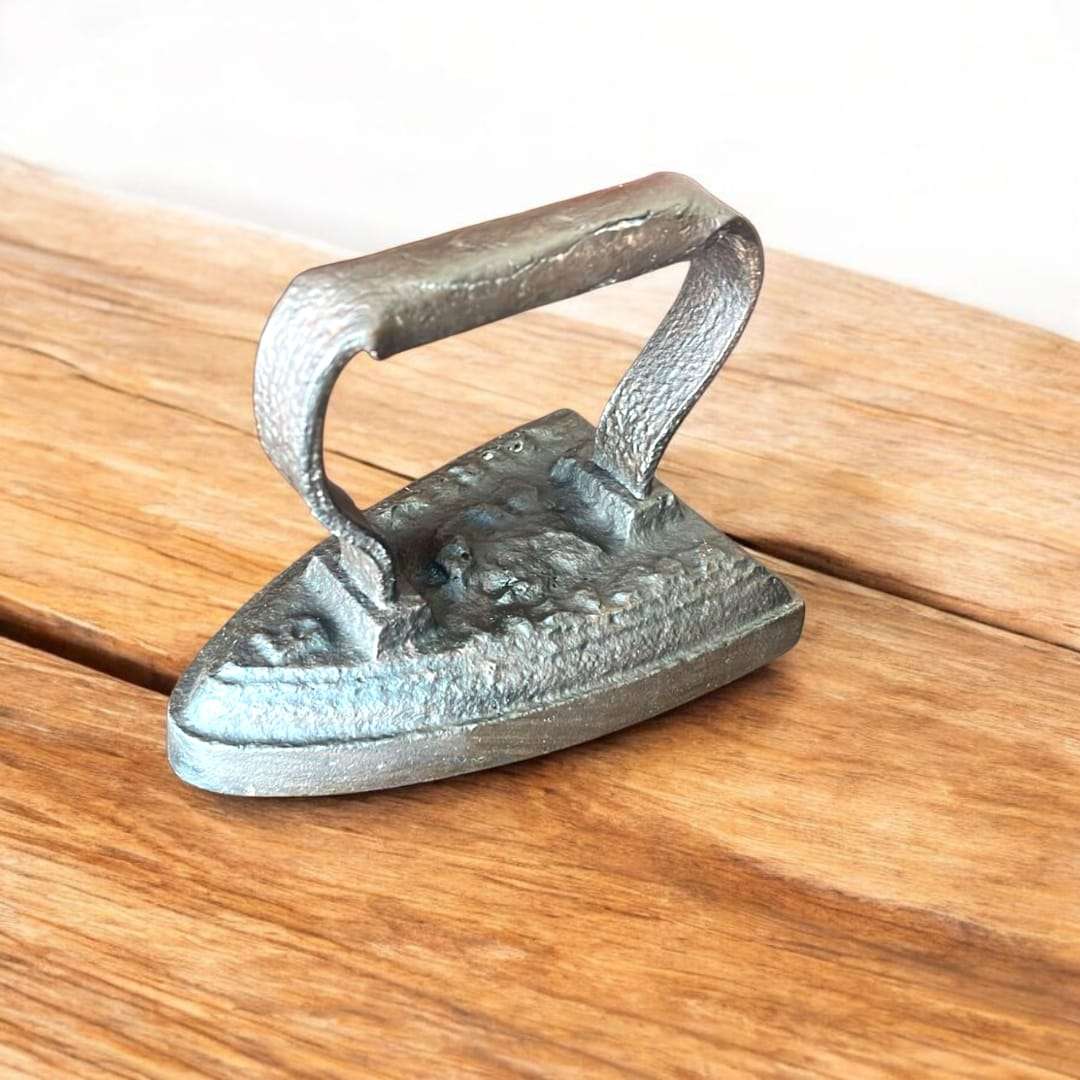 Plancha antigua de hierro fundido con acabado rústico sobre mesa de madera, ideal para decorar vintage en espacios del hogar.