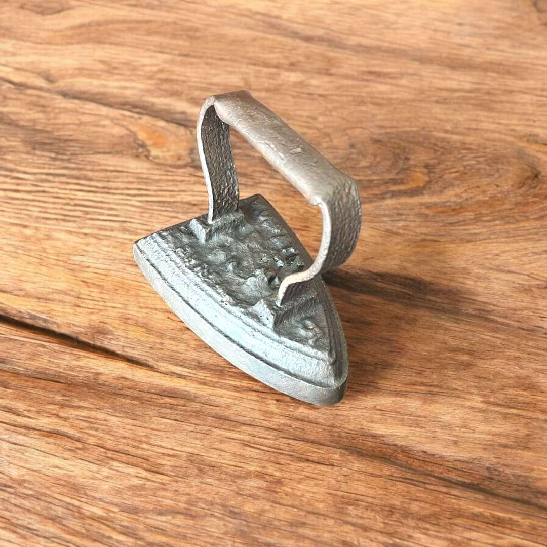 Plancha antigua de hierro fundido con acabado rústico sobre mesa de madera, ideal para decorar vintage en espacios del hogar.