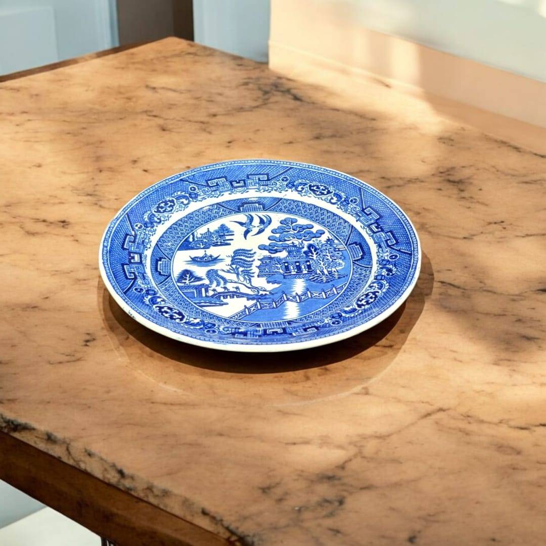 Plato redondo Willow de porcelana inglesa con estampado azul, colocado en mesa de mármol. Pieza decorativa para coleccionistas de diseño antiguo.