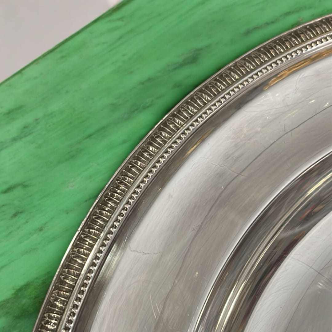 Detalle del borde decorativo de la bandeja redonda de metal plateado, resaltando su diseño clásico y elegante.