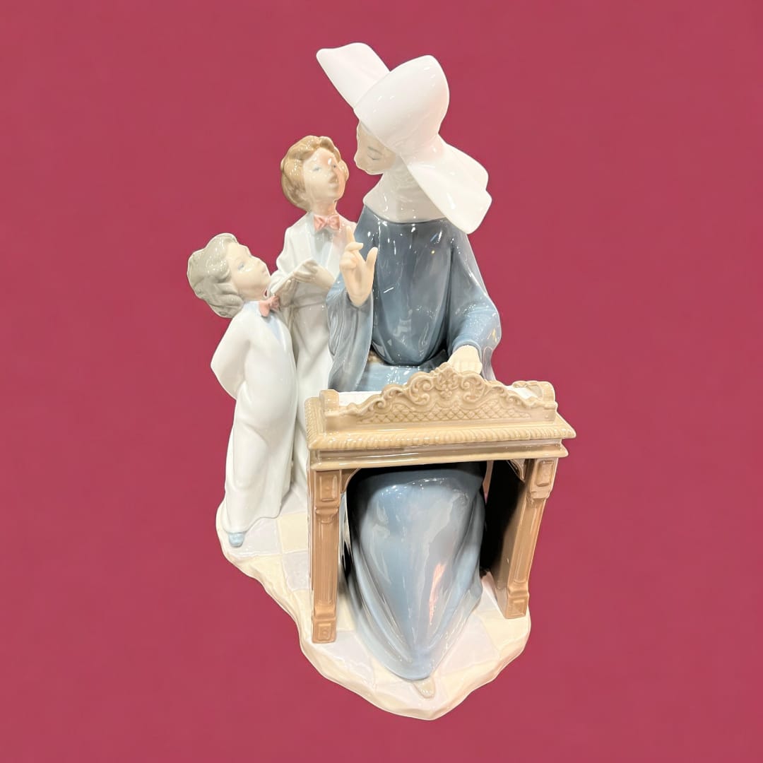 Figura de porcelana Lladró representando una monja tocando el piano con dos niños. Diseño refinado, ideal para decoración clásica y coleccionismo.