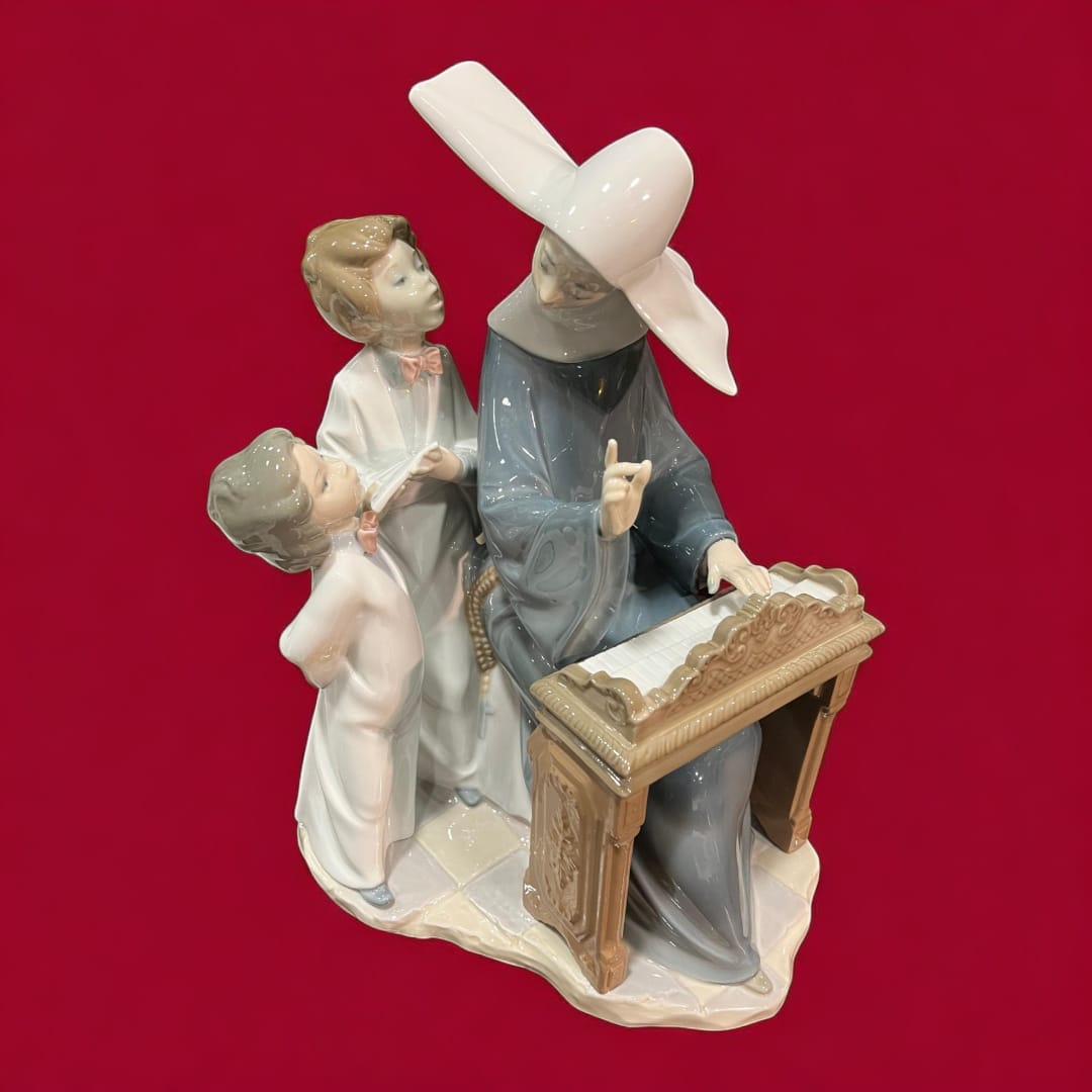 Pieza de porcelana Lladró con monja al piano y niños observando. Artesanía excepcional, perfecta para embellecer espacios con elegancia.
