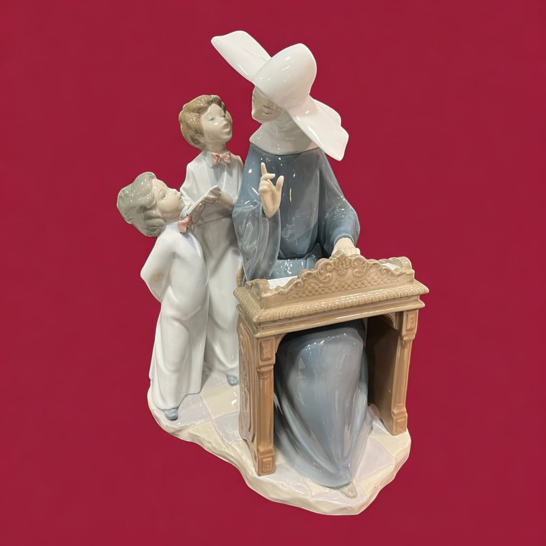 Figura de porcelana Lladró con monja tocando el piano y niños. Obra artística detallada, ideal para decoración sofisticada y coleccionismo.