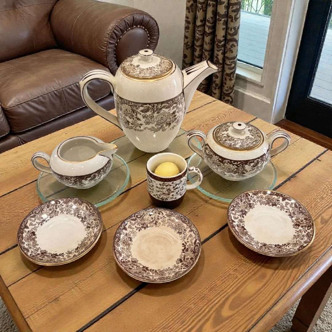 Juego de café Cartuja de Sevilla Pickman con loza decorada floral sobre mesa rústica. Elegancia histórica para decoración de hogar y coleccionistas.