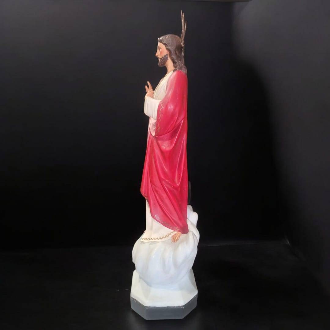 Vista lateral de la figura Sagrado Corazón de Jesús majestuosa y religiosa, mostrando detalles del manto rojo y postura bendiciente.