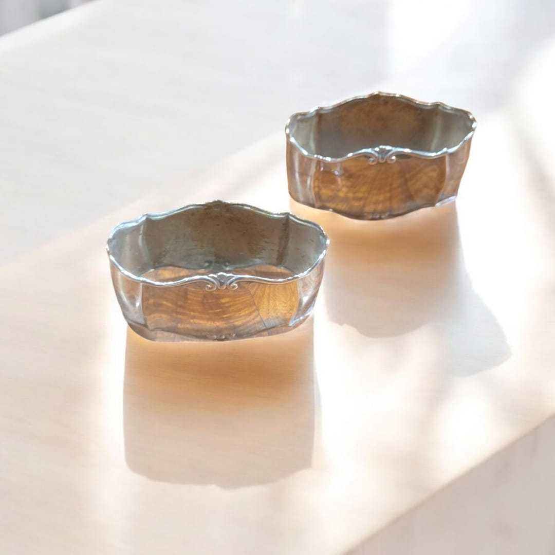 Servilleteros de metal plateado con diseño elegante sobre mesa de madera clara. Decoración clásica para mesas sofisticadas en el hogar.