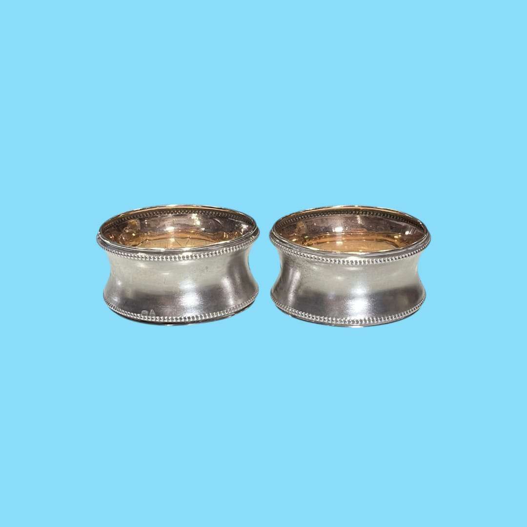 Servilleteros de metal plateado – pareja elegante sobre fondo azul.