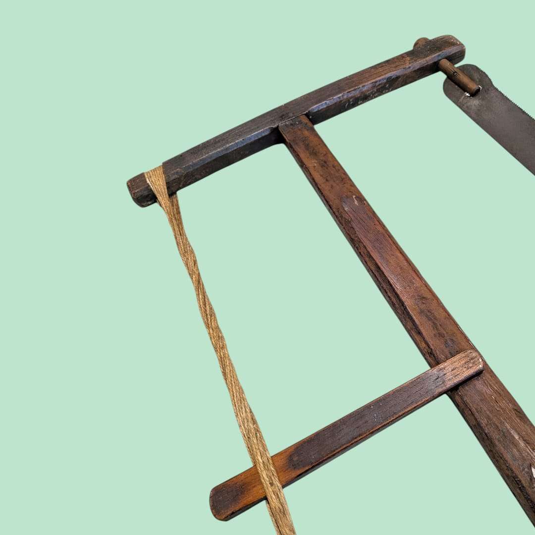 Detalle del marco y cuerda de la sierra de arco manual antigua de madera, ideal como elemento decorativo en espacios rústicos o vintage.