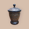 Tibor decorativo de metal con tapa ornamentada y relieves de hojas, perfecto para complementar espacios del hogar con un toque artesanal.