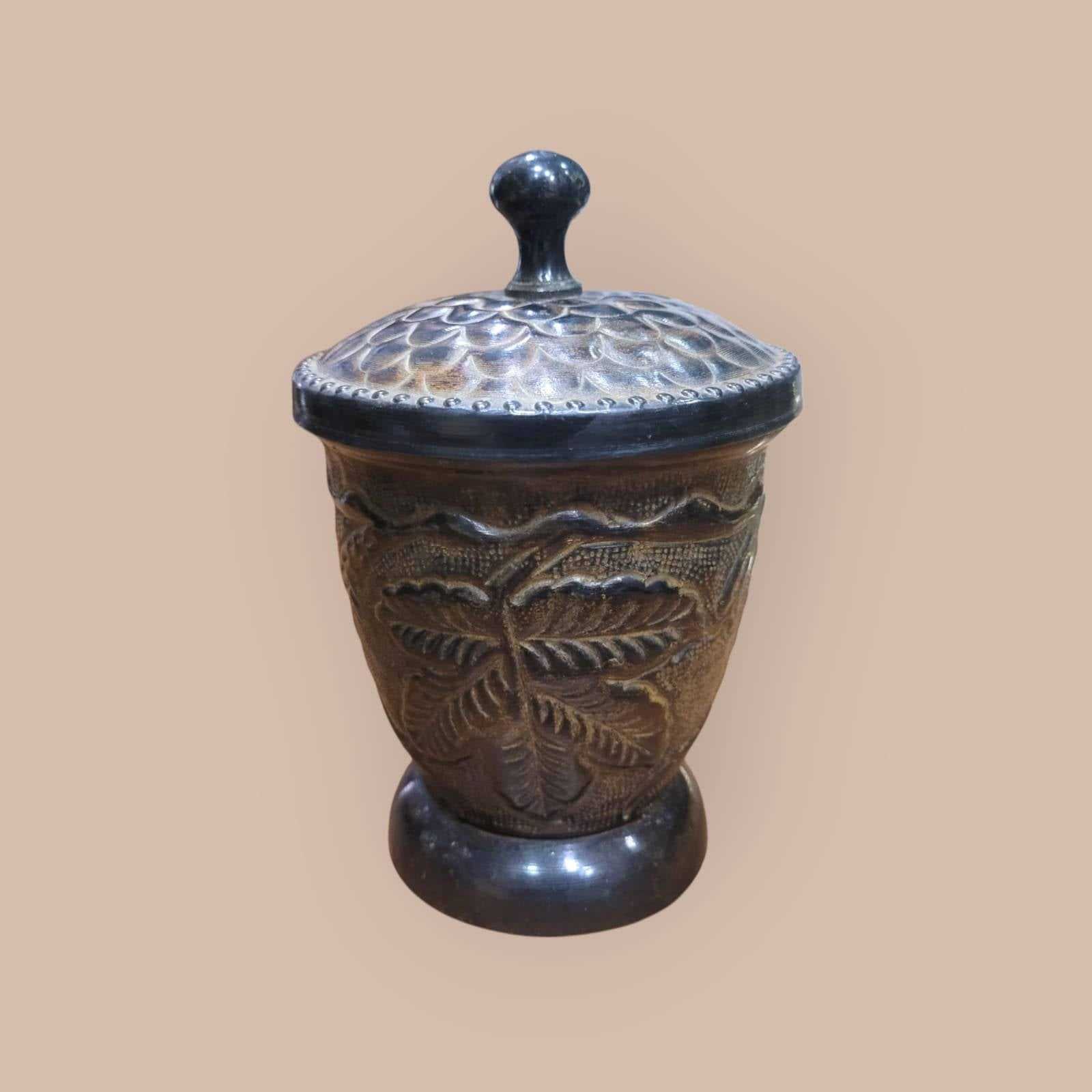 Tibor decorativo de metal con tapa ornamentada y relieves de hojas, perfecto para complementar espacios del hogar con un toque artesanal.