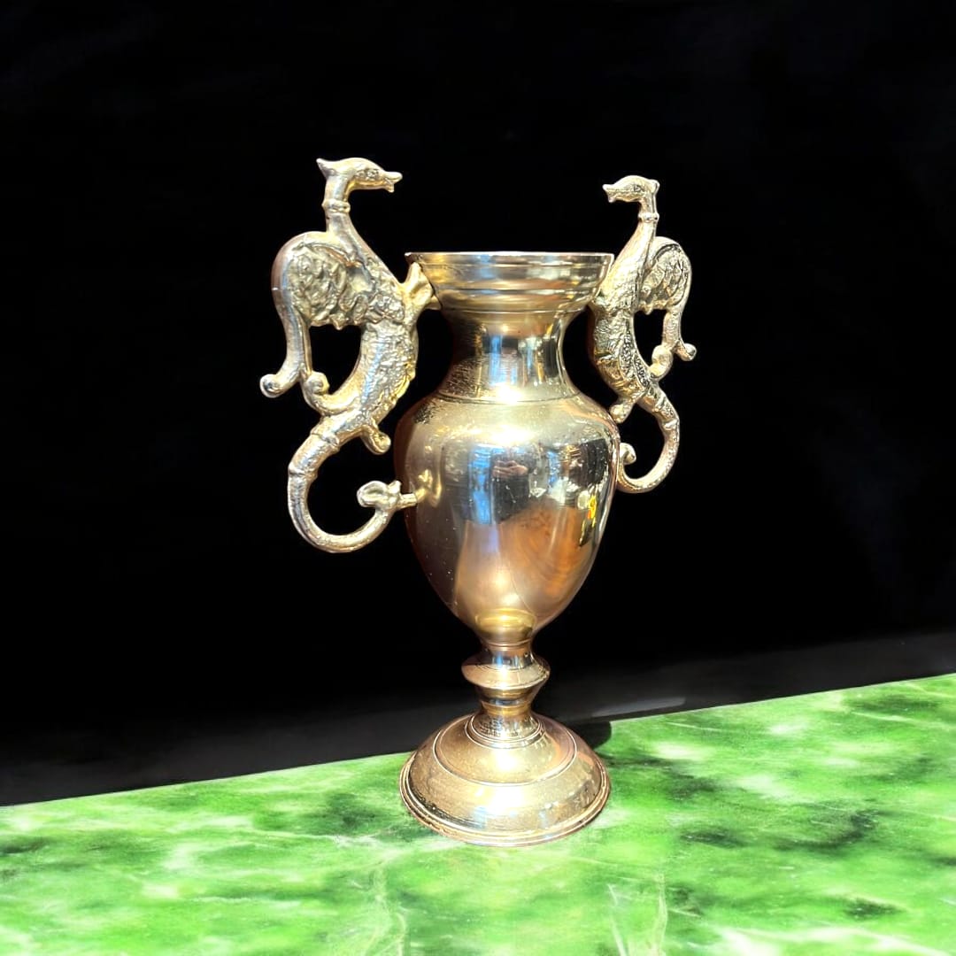 Ánfora clásica de metal dorado con dragones sobre una base de mármol verde.