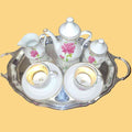 Set de café 'Tú y Yo' de porcelana con detalles dorados, diseño floral y bandeja plateada para decoración elegante.