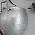 Olla de aluminio con tapa colgada en pared blanca, ideal para decoración de cocina vintage de calidad en hogar y jardín.