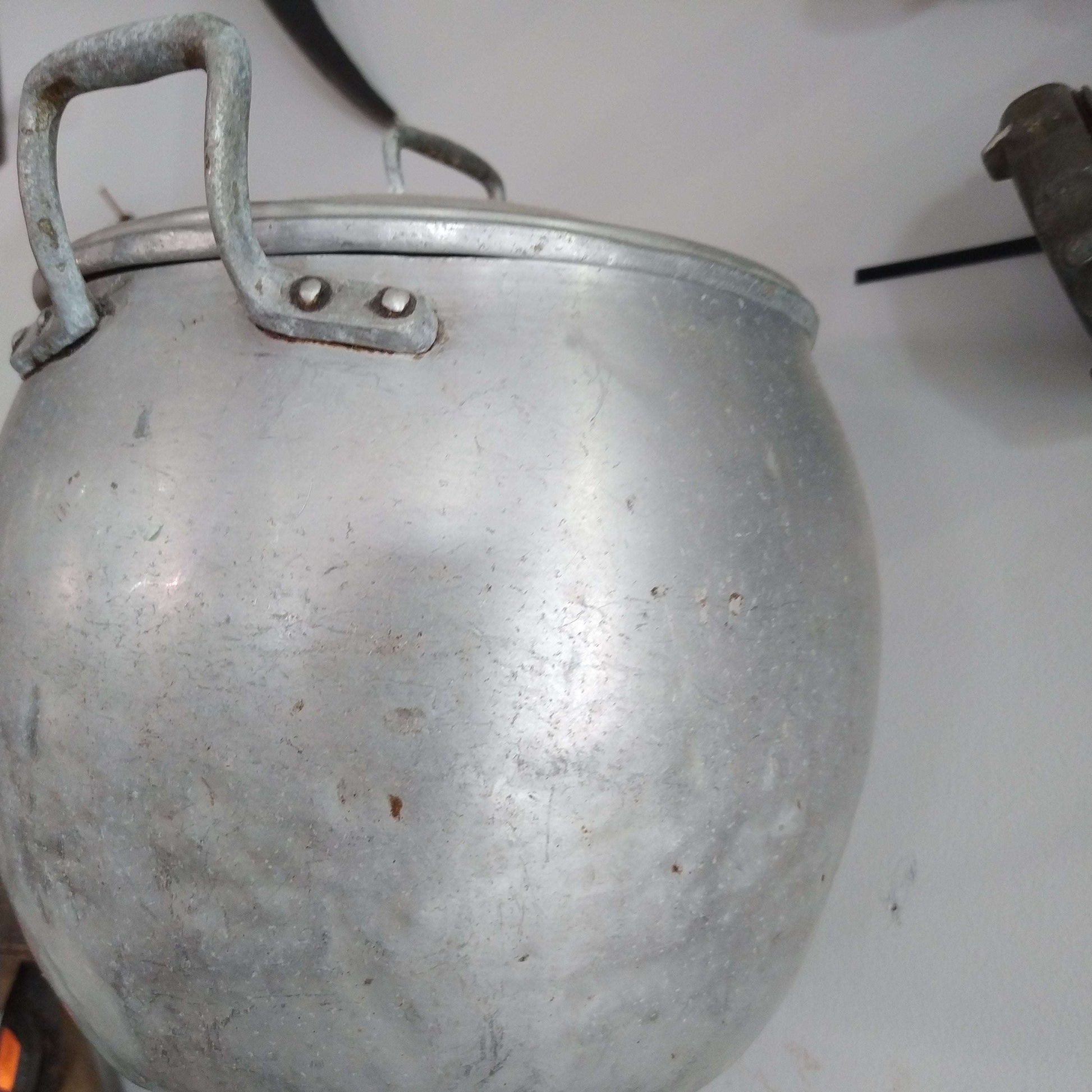 Olla de aluminio con tapa colgada en pared blanca, ideal para decoración de cocina vintage de calidad en hogar y jardín.
