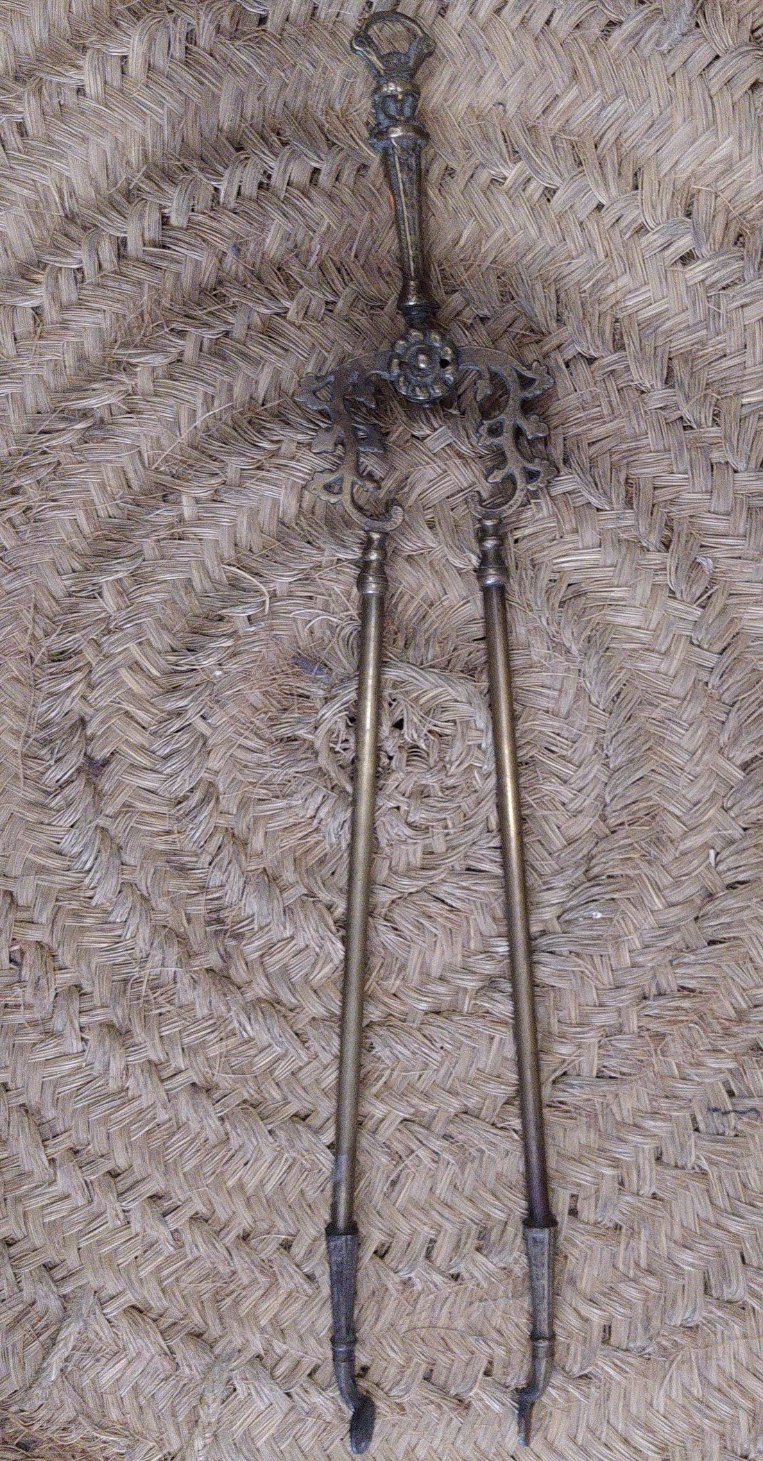 Pinza de chimenea en bronce con diseño ornamental antiguo sobre fondo de mimbre. Decoración elegante para interiores clásicos.