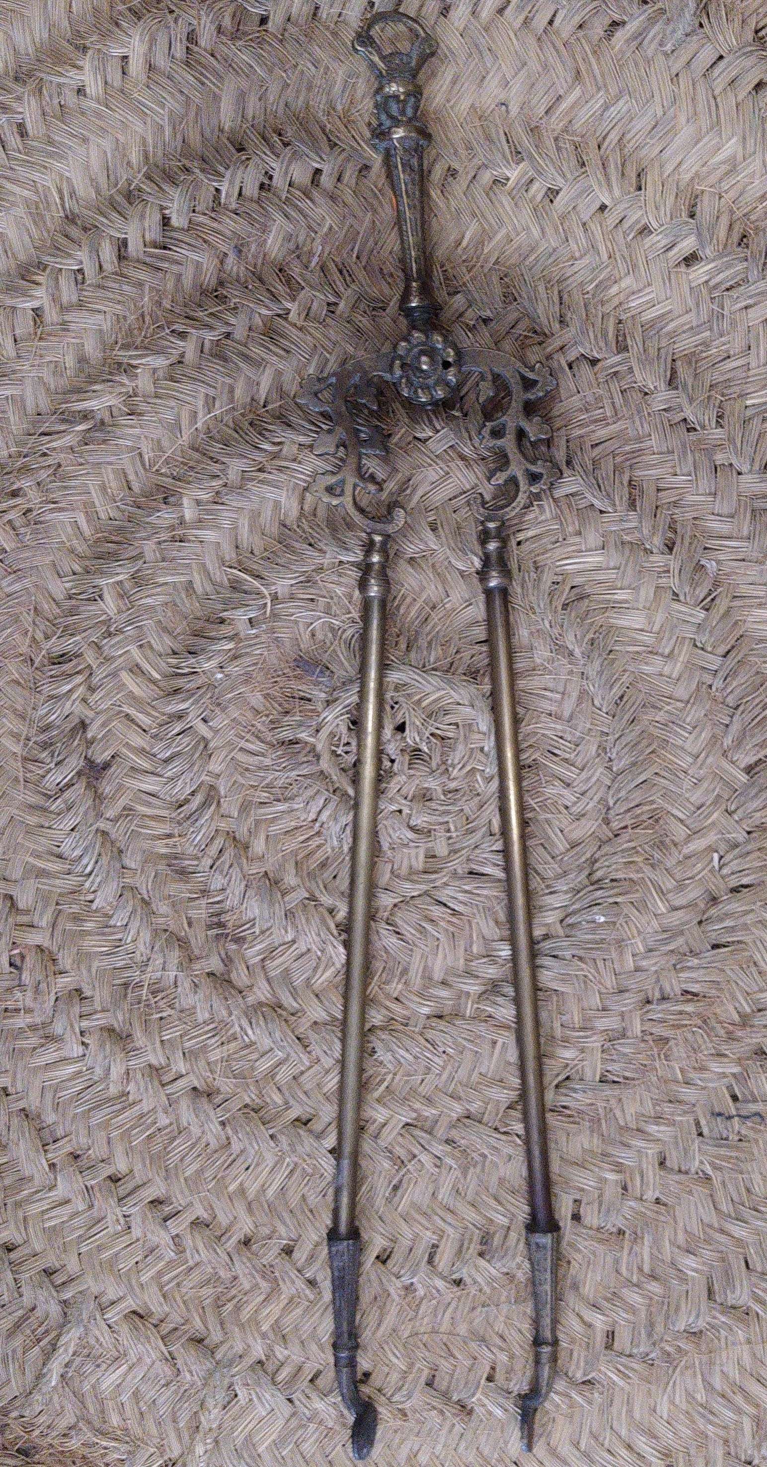 Pinza de chimenea en bronce con diseño ornamental antiguo sobre fondo de mimbre. Decoración elegante para interiores clásicos.