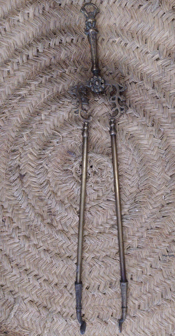 Pinza de chimenea en bronce con diseño ornamental antiguo sobre fondo de mimbre. Decoración elegante para interiores clásicos.