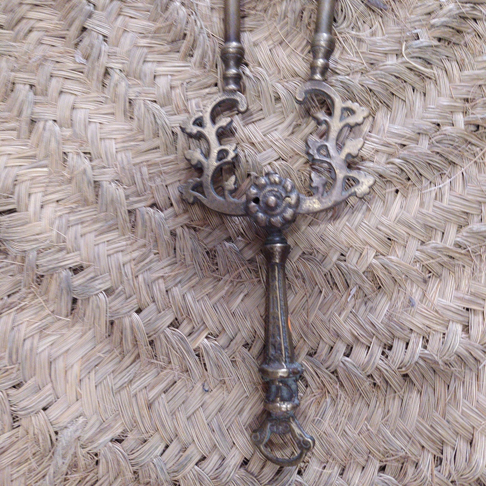 Pinza de chimenea en bronce con diseño floral y detalles ornamentales, ideal para decoración antigua y elegante en el hogar.