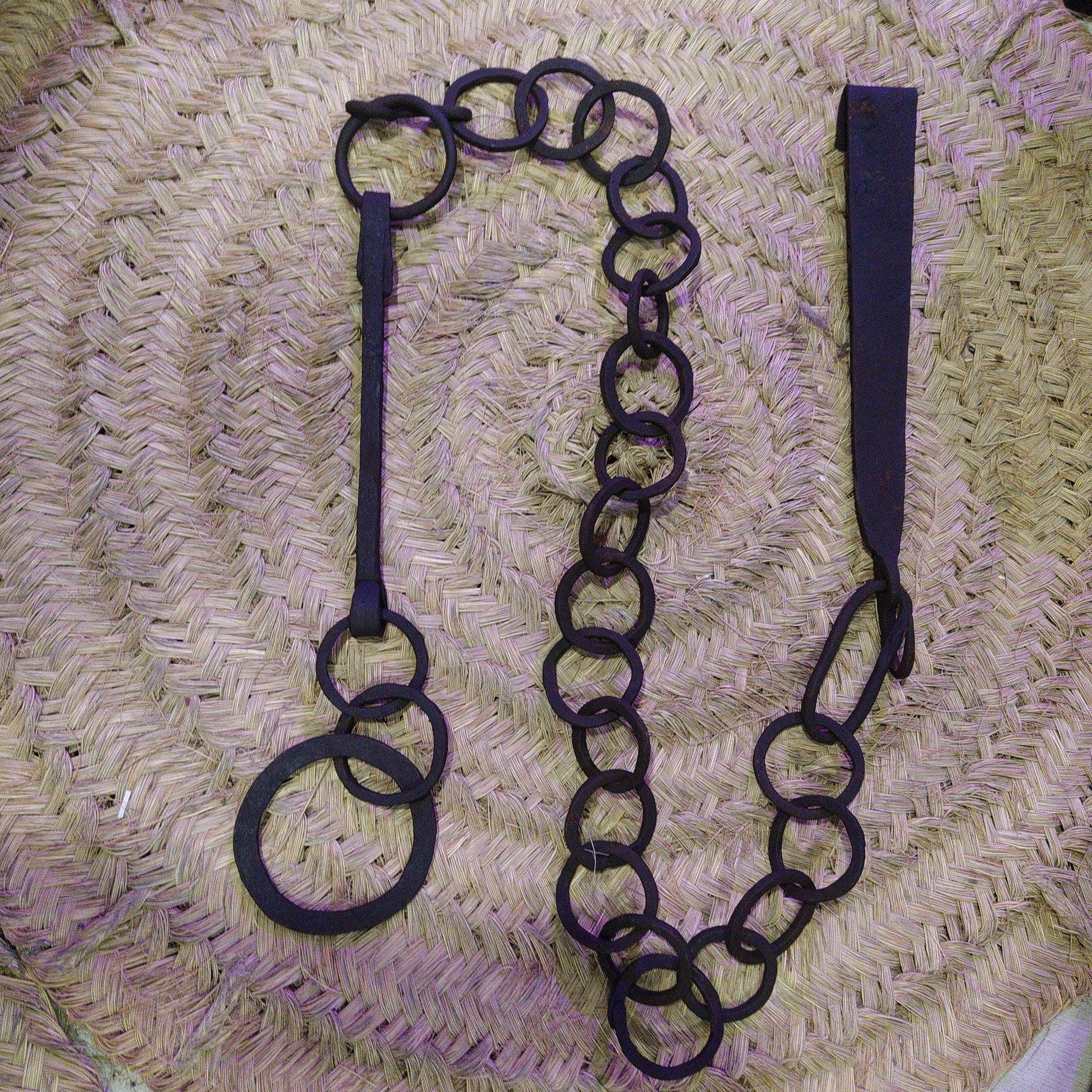 Cadena forjada - LLares de hierro forjado para colgar calderos sobre fondo de mimbre, ideal para decoración rústica de chimeneas.
