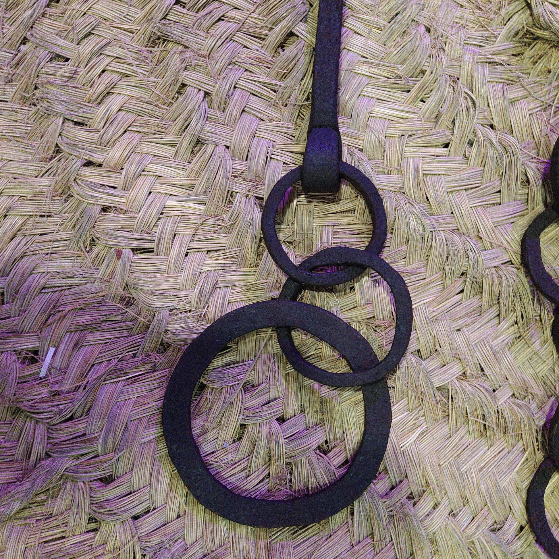 Cadena forjada de hierro con anillos entrelazados, ideal para colgar calderos en chimeneas rústicas. Decoración temática para cocinas antiguas.