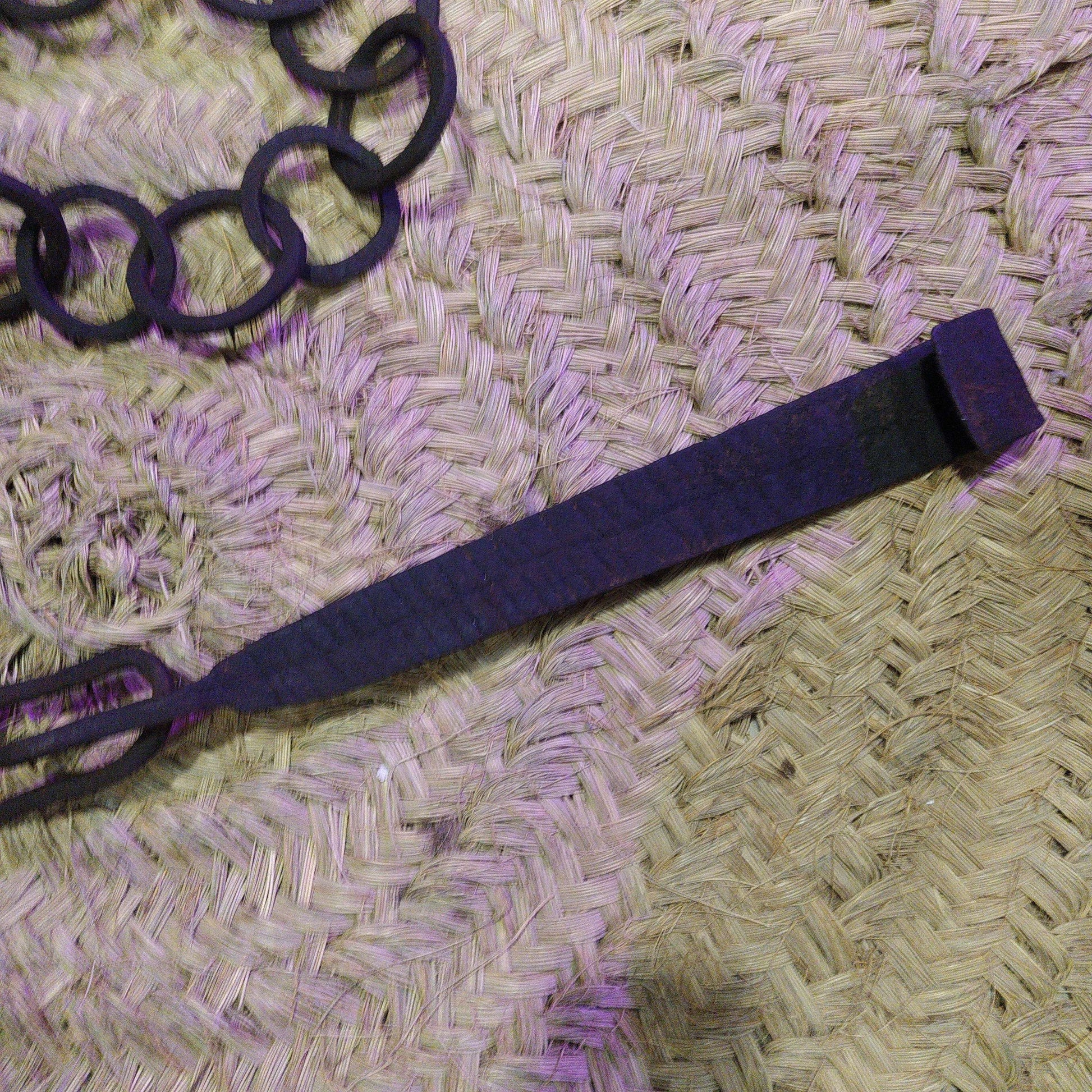 Cadena forjada - LLares de hierro forjado para colgar calderos sobre fondo de mimbre, ideal para decoración rústica de chimeneas o cocinas.