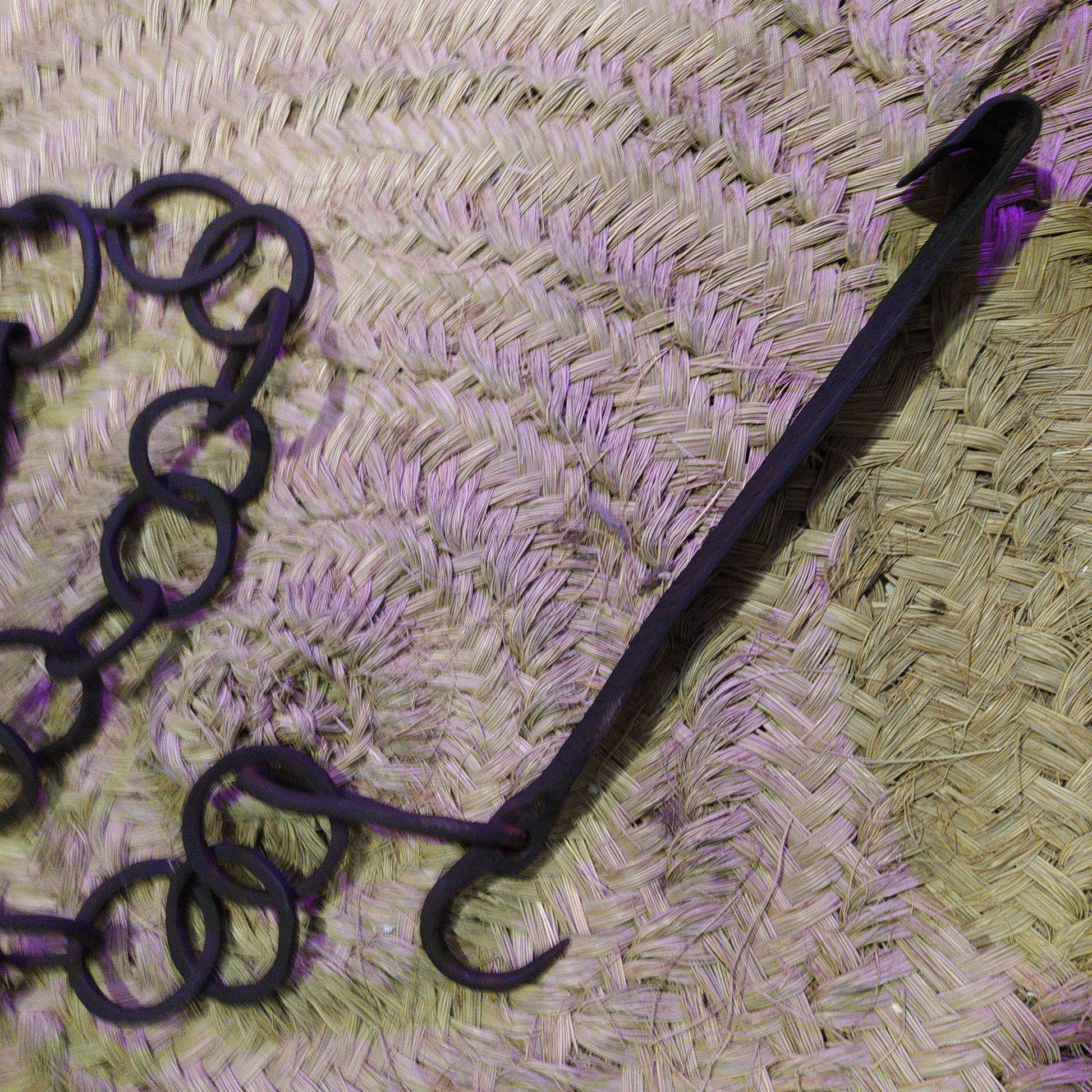 Cadena forjada - LLares de hierro forjado para colgar calderos sobre fondo de esparto, ideal para decoración rústica de chimeneas.
