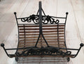Revistero de forja con detalles ornamentales y base de listones de madera, ideal para decoración rústica en hogar. Calidad excepcional en cada detalle.