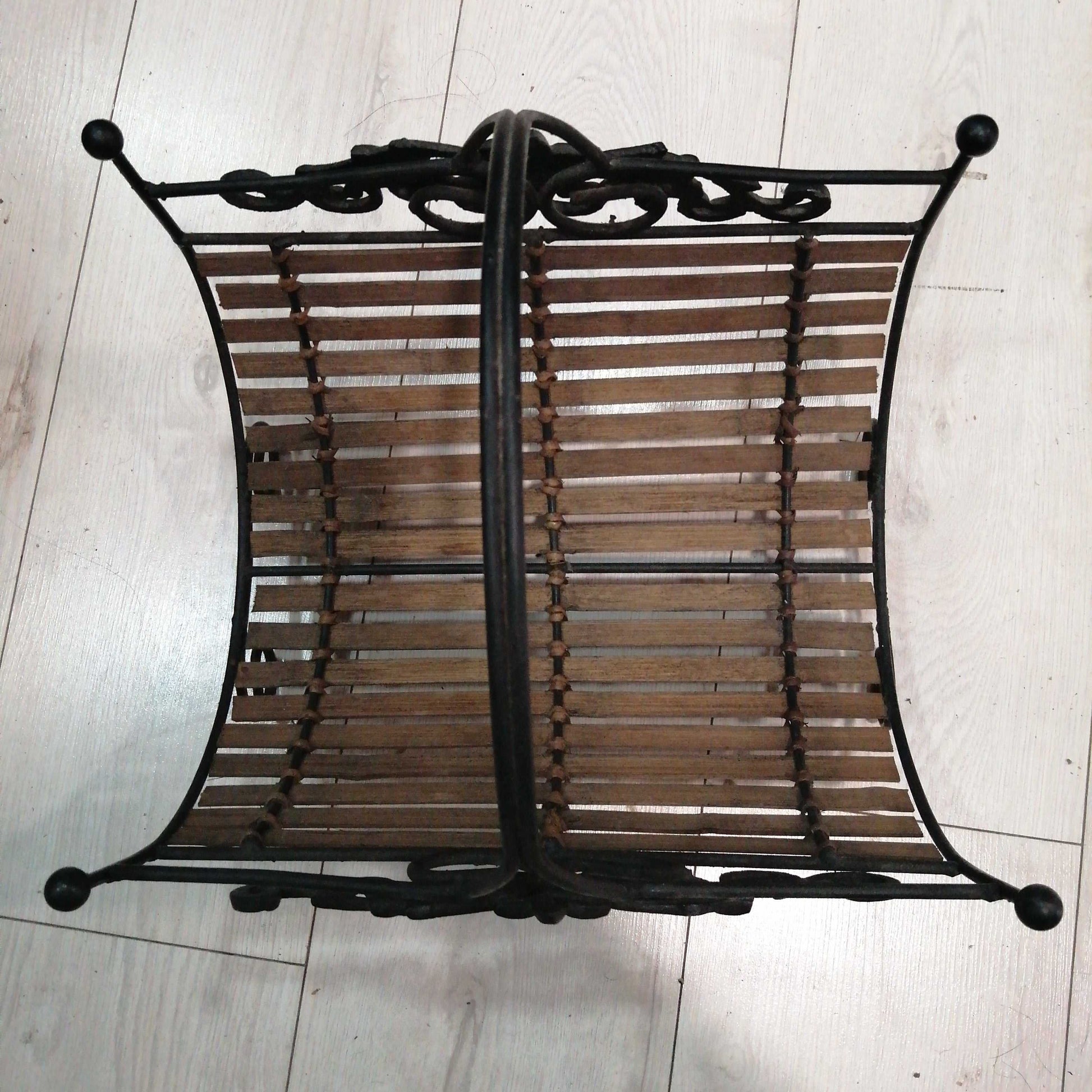 Revistero de forja con estructura metálica negra y base de listones de madera. Diseño rústico ideal para decoración de interiores elegantes.