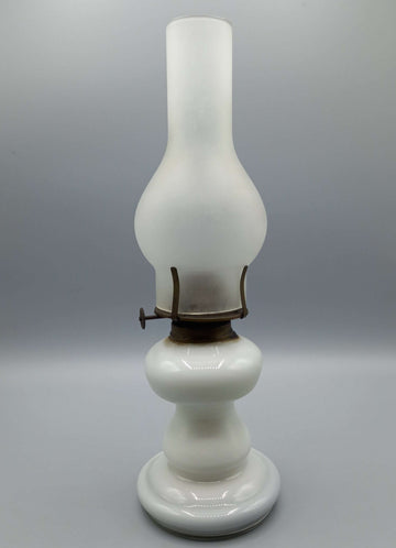 Quinqué de opalina antiguo blanco con base redonda y chimenea alta, ideal para decoración vintage en hogar. Iluminación de época exquisita.