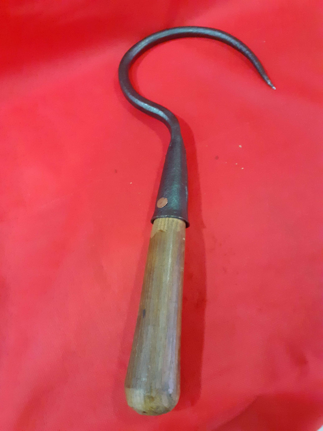 Garfio de hierro antiguo con mango de madera sobre fondo rojo, ideal para decoración rústica o coleccionistas. Disponible en Cositas Antiguas.